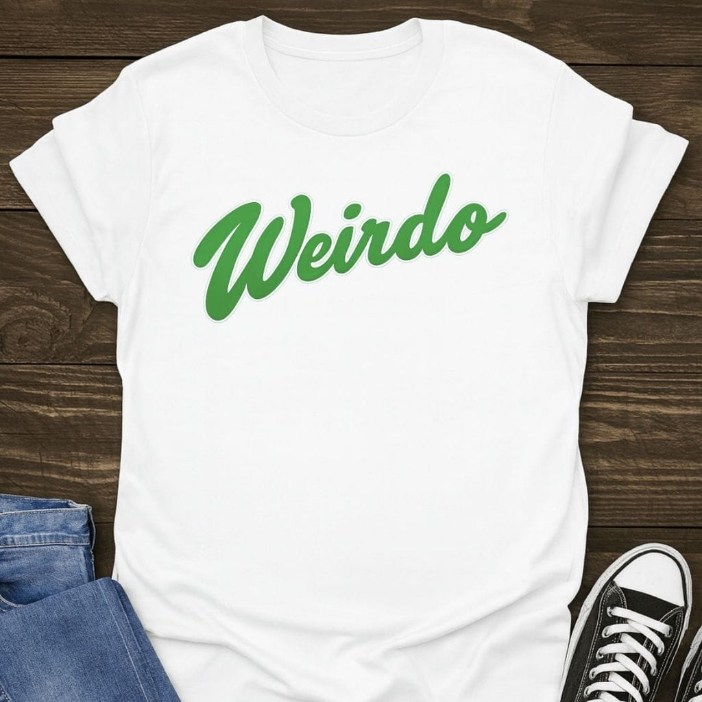 White Slogan t-shirt with green 'Weirdo' text on a wooden surface with jeans and sneakers.