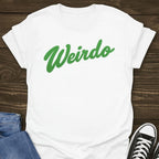 White Slogan t-shirt with green 'Weirdo' text on a wooden surface with jeans and sneakers.